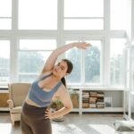 A plus size woman stretches energetically in a sunlit room, promoting body positivity and wellness.