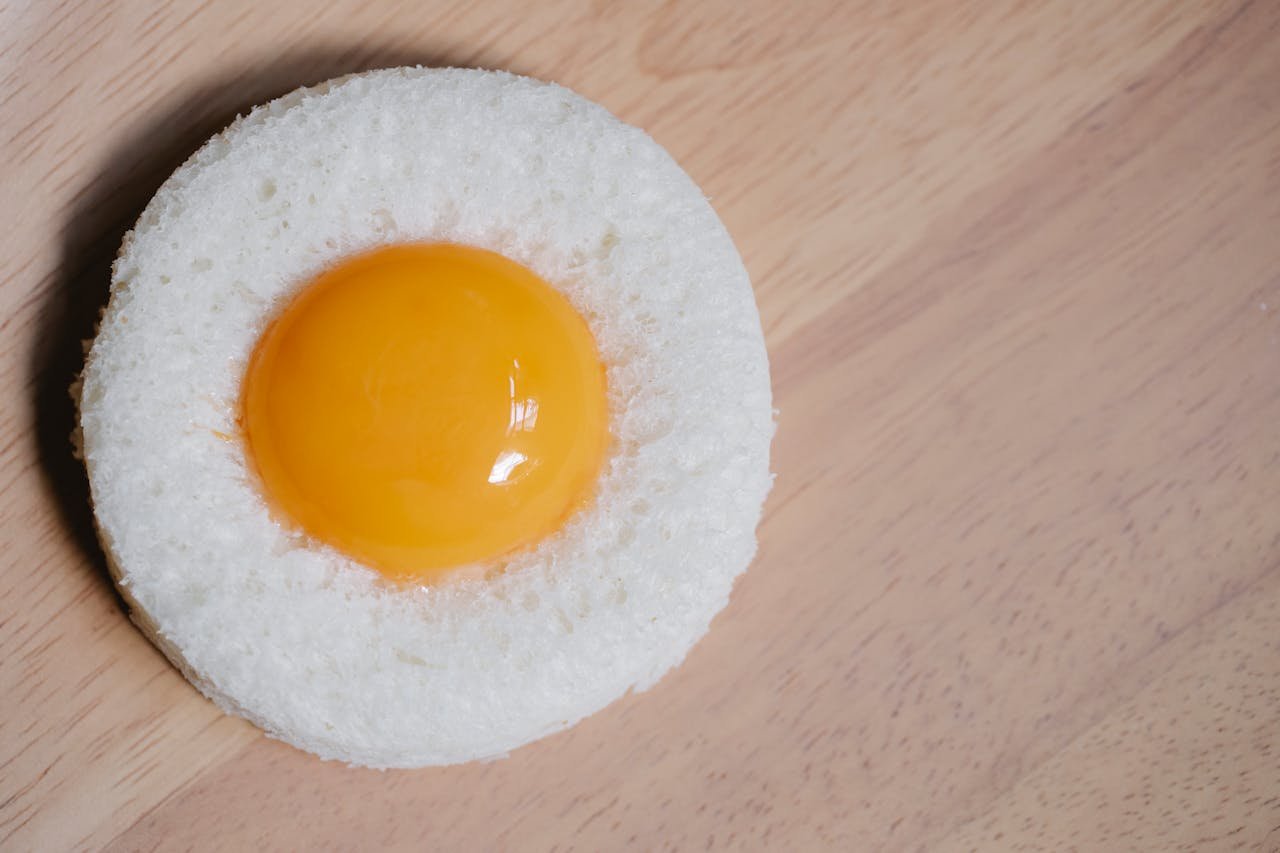 A close-up of a raw egg yolk nestled on a slice of fresh bread on a wooden surface.